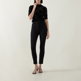 Model wearing Ted Baker black slim-leg trousers, styled with a black floral velvet top and strappy heels.