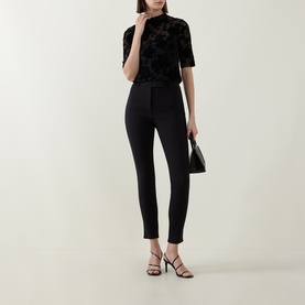 Model wearing Ted Baker black slim-leg trousers with velvet floral top, black mini bag and strappy heeled sandals.