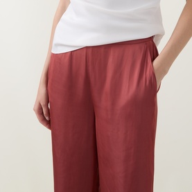 Model wearing Ted Baker Burnt Red wide-leg trousers with elasticated waist, styled with a white top.