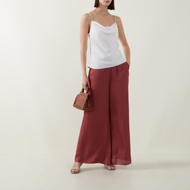 Model wearing Ted Baker Burnt Red wide-leg trousers, styled with a white cami top, small brown bag and strappy sandals.