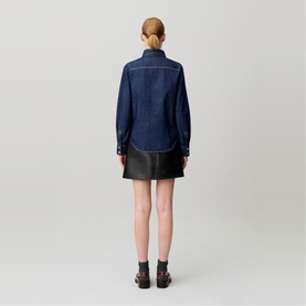Model wearing Claude Pierlot blue denim shirt with contrast stitching, styled with black mini skirt and chunky black shoes, back view.