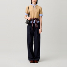 Model wearing Claude Pierlot Stripe Hybrid Sweater in clear, with striped poplin collar and bow tie, styled with wide-leg navy trousers and green bag.