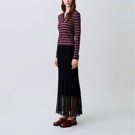 Model wearing Claude Pierlot Rib Knit Skirt in black, maxi length with sheer fringed hem, styled with a striped knit top and brown loafers.