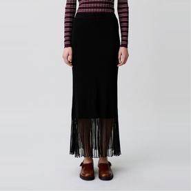 Model wearing Claude Pierlot Rib Knit Skirt in black, maxi length with fringe hem, styled with a striped long-sleeve top and brown leather shoes.