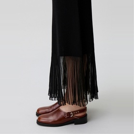 Model wearing Claude Pierlot Rib Knit Skirt in black, maxi length with sheer fringed hem, styled with tan leather buckle loafers.
