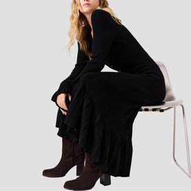 Model wearing Maje Womens French Dress in red, styled with dark brown knee-high boots, seated on a chair.