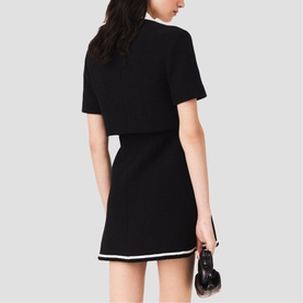 Model wearing black short-sleeve knit top and mini skirt set with white contrast trim, holding black heels, rear view.
