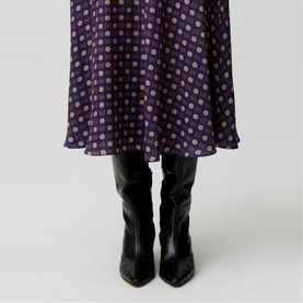 Model wearing Claude Pierlot navy print midi skirt with gold dot pattern, styled with black knee-high leather heeled boots.