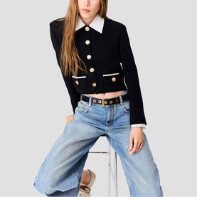 Model wearing Maje red cropped jacket with white collar, gold buttons, and white pocket trim, styled with light blue jeans and a belt.