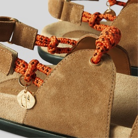 Claude Pierlot brown suede sandals with orange braided rope lacing and gold charm detail, close-up view.