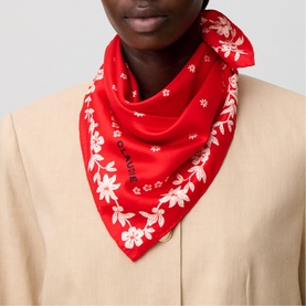 Model with red silk scarf featuring white floral print, tied at the neck, worn over a beige blazer