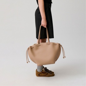 Model carrying Claude Pierlot bag in clear beige, large tote silhouette with drawstring detail and short top handles, styled with black midi skirt