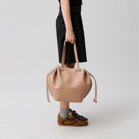 Model carrying Claude Pierlot bag in clear beige leather, with drawstring detail and double top handles, styled with black culottes and tan trainers