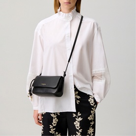 Model carrying black crossbody bag with gold-tone hardware and adjustable strap, styled with white blouse and floral trousers