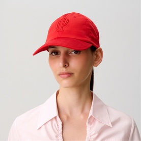 Model wearing Claude Pierlot red baseball cap with tonal embroidered logo, styled with a light pink collared shirt.