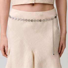 Model with silver coin-link chain belt worn over cream quilted midi skirt and matching crop top