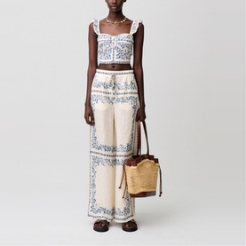 Model wearing cream and blue paisley wide-leg trousers with matching crop top, carrying a small brown bucket bag with woven detail.