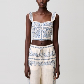 Model wearing white and blue floral embroidered crop top with ruffle straps, styled with printed linen trousers