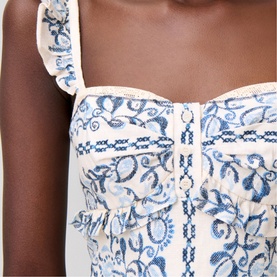 Model wearing white and blue floral embroidered corset top with ruffle straps and front hook-and-eye fastening detail