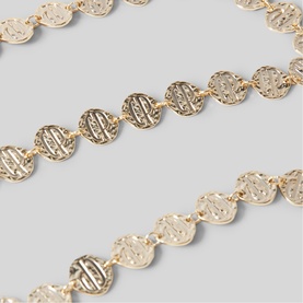 Claude Pierlot metallic gold chain belt featuring engraved circular disc links, laid flat on grey surface