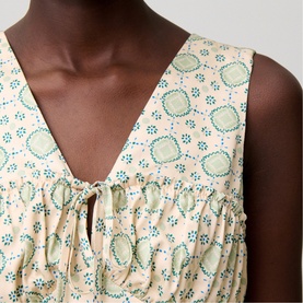 Model wearing cream sleeveless top with green geometric and floral print, V-neck with tie detail and gathered front panel