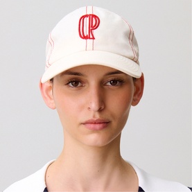 Model wearing cream baseball cap with red CP monogram embroidery and contrast red stitching detail