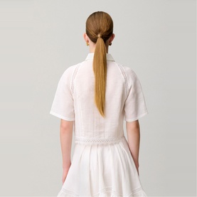 Model wearing white short-sleeve cropped top with textured fabric detail, styled with a white skirt, rear view