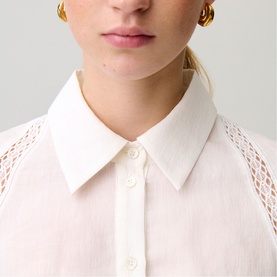 Model wearing white shirt with sheer lace mesh sleeves, styled with gold hoop earrings. Close-up collar detail shot.