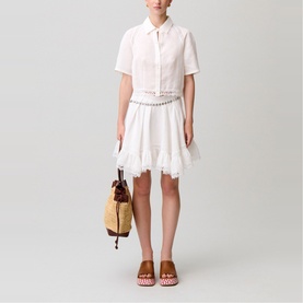 Model wearing white short-sleeve shirt dress with lace trim and tiered skirt, styled with woven bag and brown mule sandals