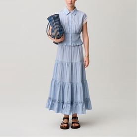 Model wearing Claude Pierlot light blue tiered maxi shirt dress with cap sleeves, styled with a navy clutch bag and black sandals