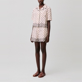 Model wearing cream polka dot short-sleeve shirt and matching shorts with scalloped hem, styled with brown loafers