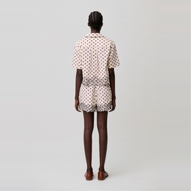 Model wearing cream polka dot short-sleeve shirt and matching shorts, styled with tan sandals, rear view