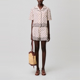 Model wearing cream and red polka dot short-sleeve shirt and shorts set, styled with a woven bucket bag and brown loafers