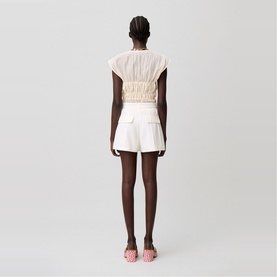 Model wearing cream ruched sleeveless top and white tailored shorts, styled with pink flat sandals, rear view