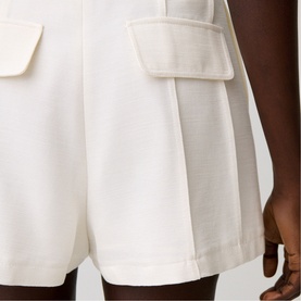 Model wearing cream tailored shorts with structured patch pockets and wide-leg silhouette, close-up detail view