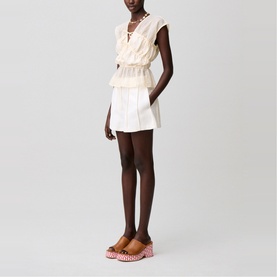 Model wearing cream sleeveless ruffled mini dress with lace trim, styled with pink patterned platform sandals