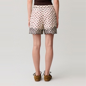 Model wearing Claude Pierlot light print shorts with floral border detail, styled with a dark top and tan lace-up shoes, rear view.