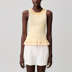 Model wearing pale yellow sleeveless knit top with floral neckline embroidery and pleated frill hem, styled with white shorts