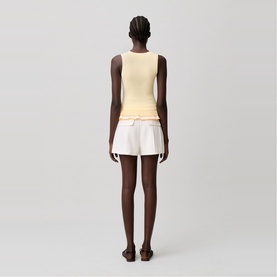 Model wearing a pale yellow sleeveless top, styled with white drawstring shorts and brown flat sandals, seen from behind.