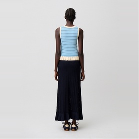 Model wearing Claude Pierlot black pleated midi skirt, styled with a light blue striped knit tank top, rear view