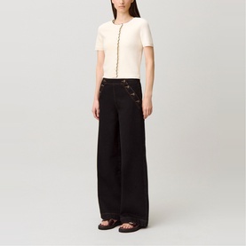 Model wearing black wide-leg trousers with gold button detail, styled with cream short-sleeve knit top and black flat sandals