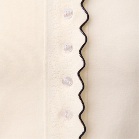 Cream knit fabric with black ric-rac trim detail and clear buttons along placket, close-up view