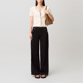 Model wearing black wide-leg trousers with gold-tone button details, styled with a cream knit top and black sandals, carrying a tan shoulder bag