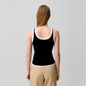 Model wearing Claude Pierlot black sleeveless tank top with white contrast trim, styled with beige trousers. Back view.