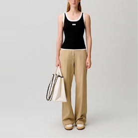Model wearing Claude Pierlot black and white sleeveless ribbed top with beige wide-leg trousers, styled with cream tote bag and tan sandals.