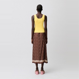 Model wearing dark brown floral midi skirt with border hem, styled with yellow vest top and pink sandals, back view
