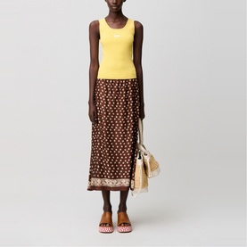 Model wearing brown floral midi skirt with yellow tank top, styled with patterned mules and a woven bag