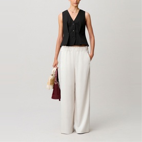 Model wearing Claude Pierlot clear wide-leg trousers with elasticated waist, styled with black waistcoat, carrying burgundy bag.