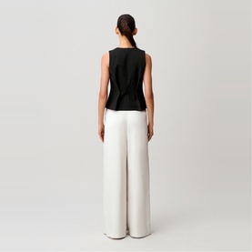 Model wearing Claude Pierlot sleeveless black top with white wide-leg trousers, rear view on grey background