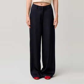 Model wearing navy wide-leg tailored trousers with pressed front pleats, styled with red shoes